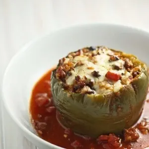 A white bowl with a cooked green pepper stuffed with beef vegetables and rice and topped with melted cheese.