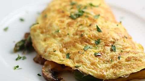 White plate with folded omelete made with asparagus and mushrooms.