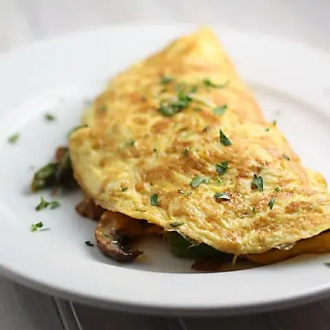 White plate with folded omelete made with asparagus and mushrooms.
