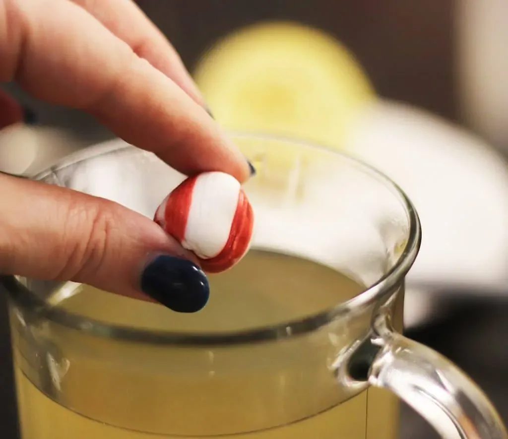 A piece of soft peppermint going into a cup of hot toddy for cough.