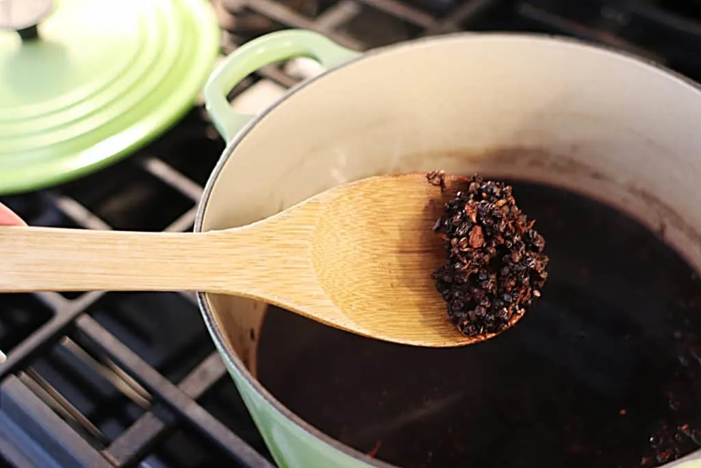 A spoon holding cooked elderberries over a green pot