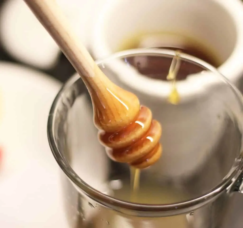 A wood honey dripper with honey dripping into a glass cup for a hot toddy for cough.